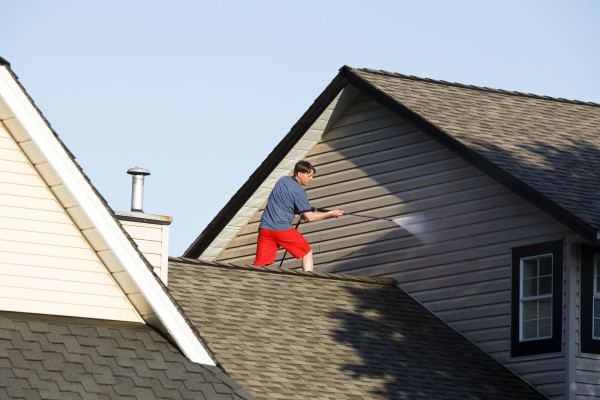 Man on the roof of a house pressure washing the vinyl siding.
